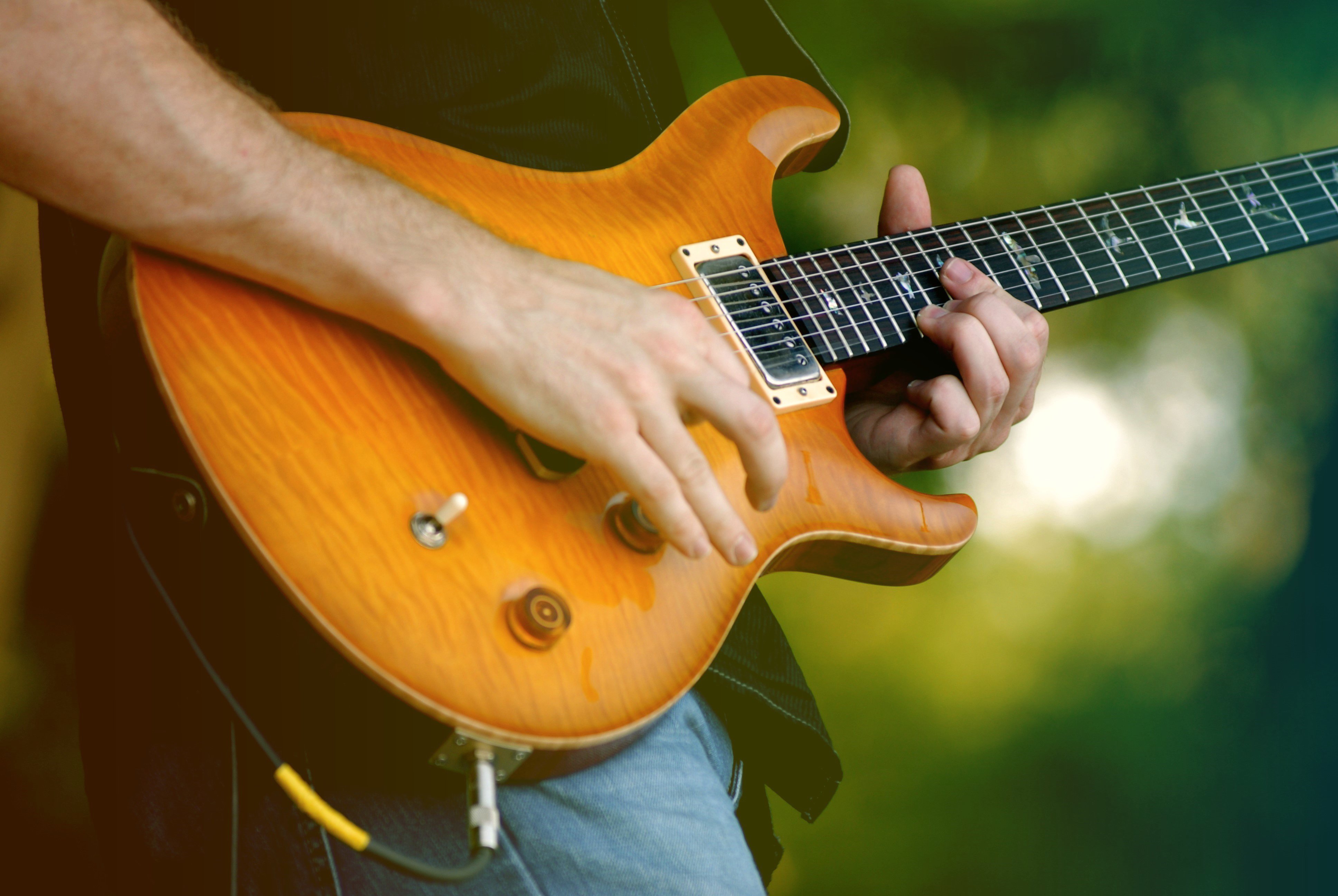 Close-up photograph of musician playing guitar at an outdoor festival.