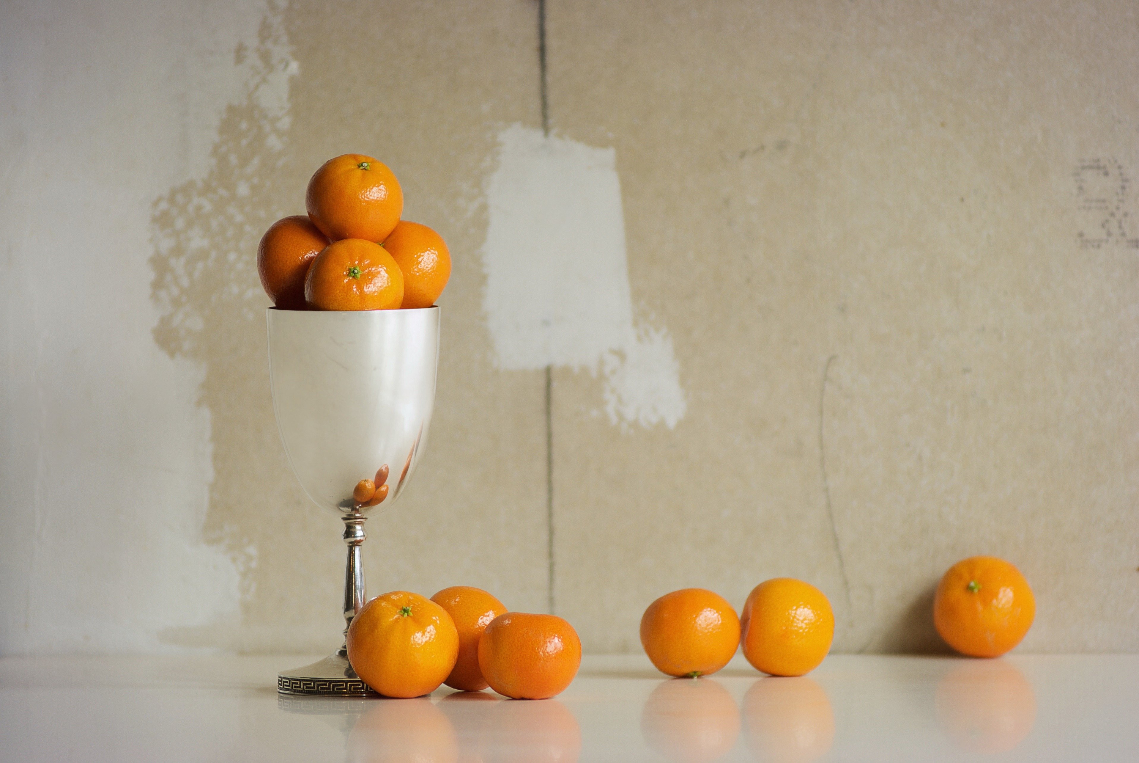 Still life art. Photograph of oranges in a silver goblet against a neutral background in window light.